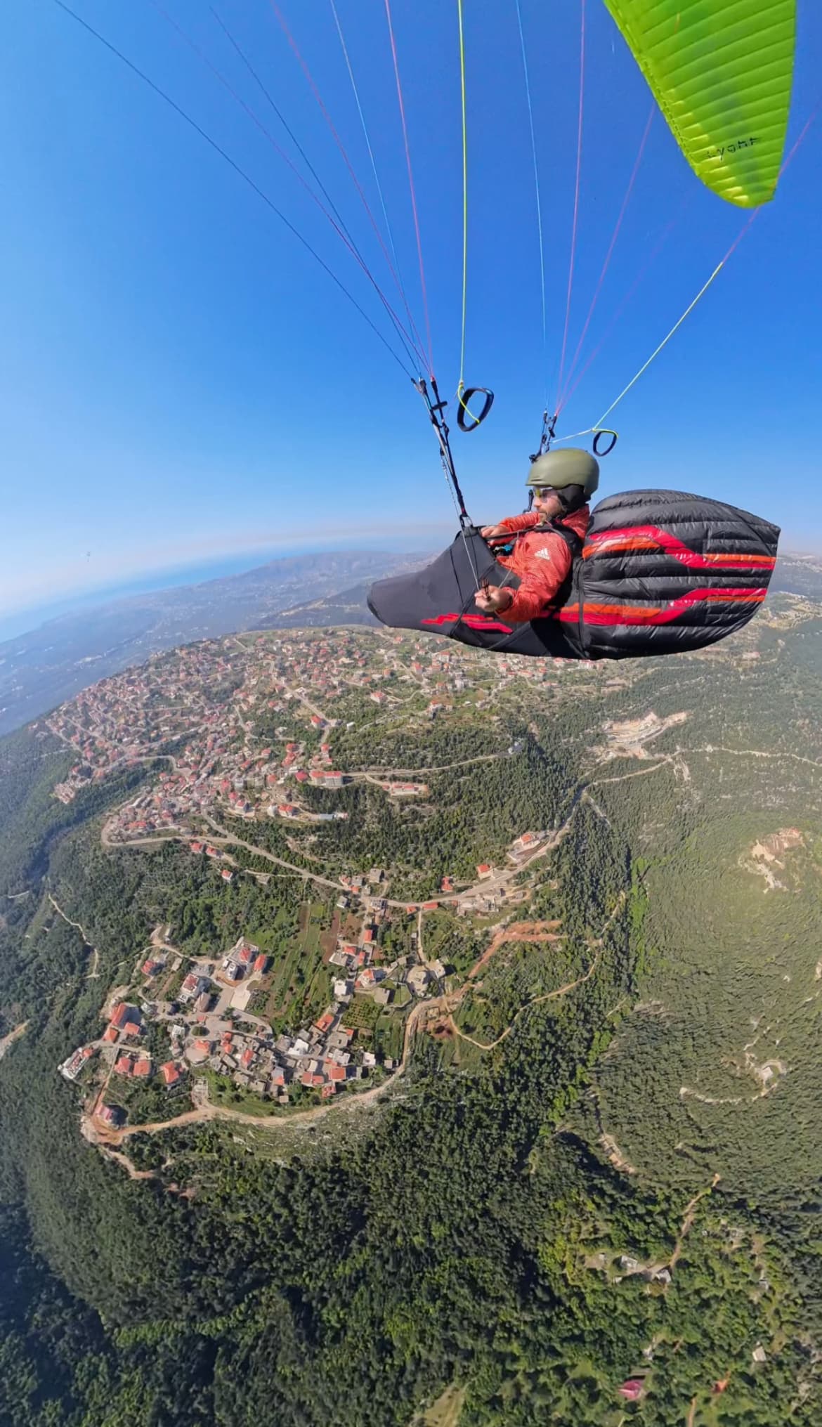 Paraglider above green Miziara mountain ridge and Lebanese village rooftops
