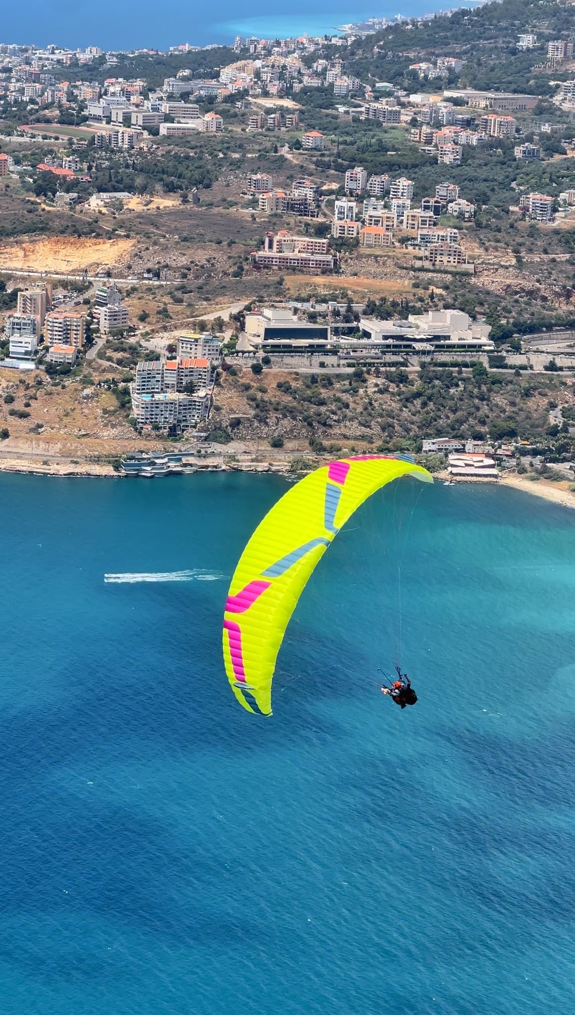 Yellow paraglider wing soaring above turquoise Jounieh Bay, Lebanon